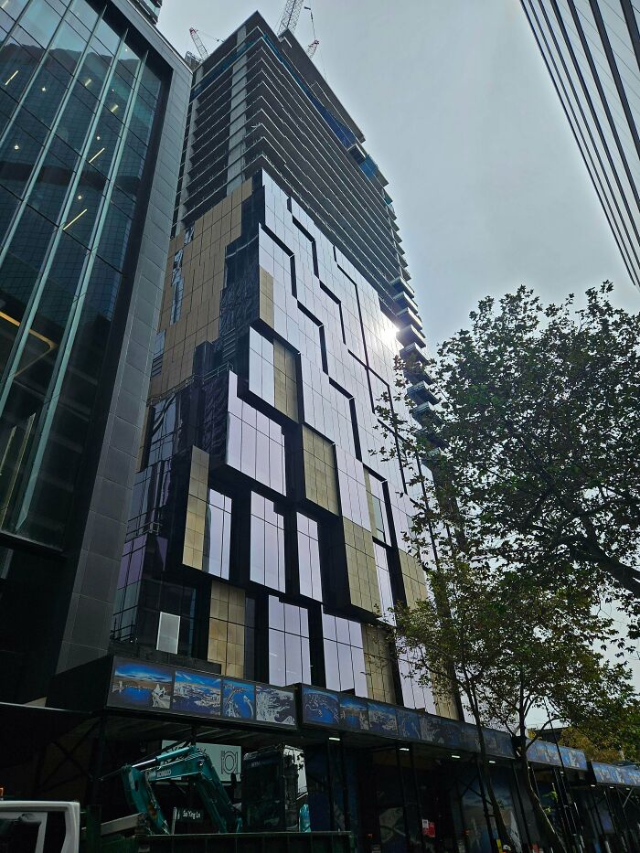 A striking, modern building with an impressive geometric glass and gold facade under construction, showcasing inspiring architecture.