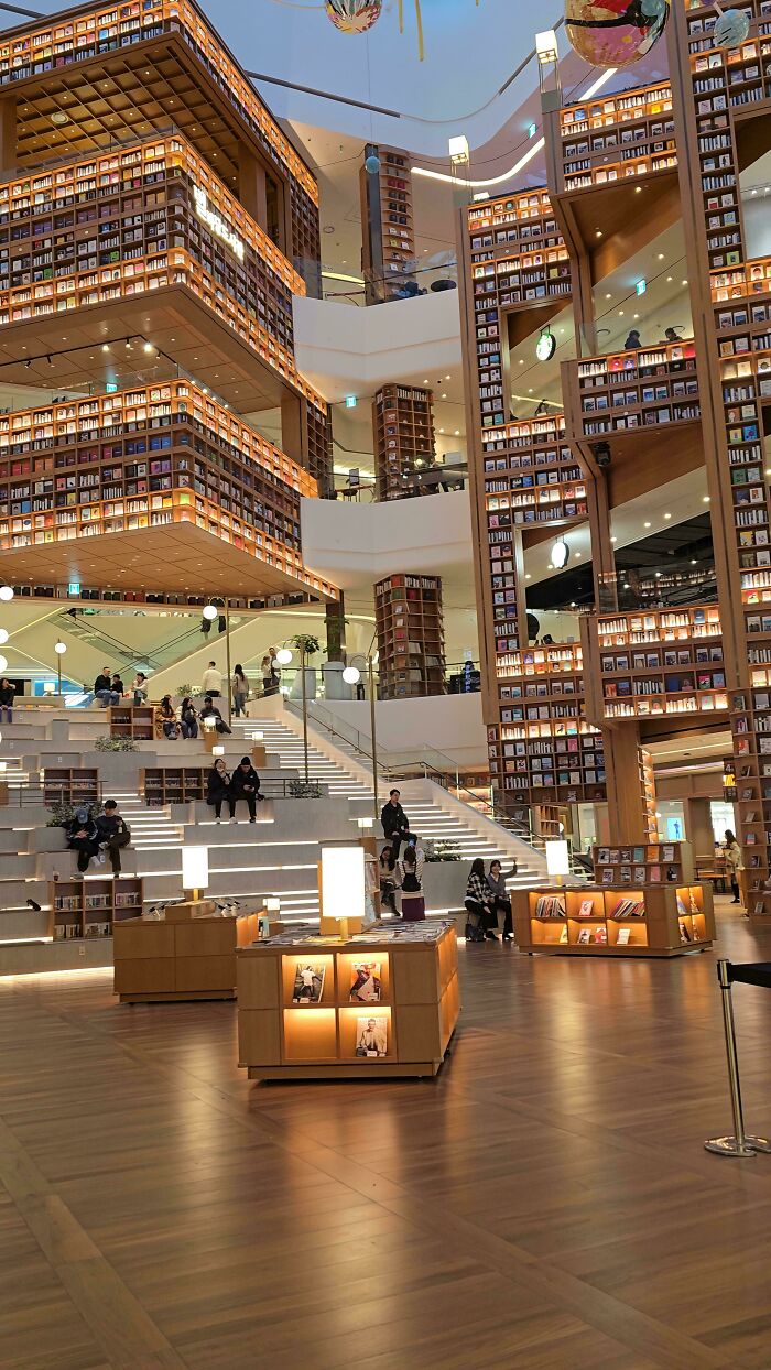 An impressive library interior showcasing towering bookshelves, multiple levels, and people sitting on wide steps. Architecture lovers will appreciate this design.