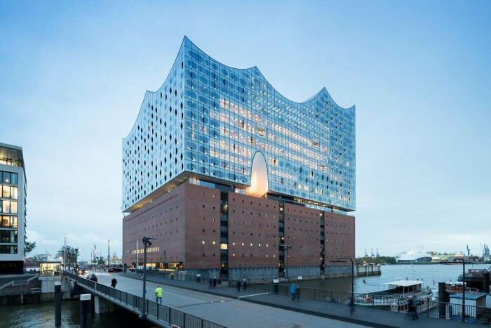 Impressive building with a wavy glass top and brick base by the water, showcasing unique architecture.