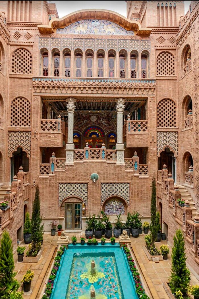 An impressive building with intricate brickwork, colorful tiles, stained glass, and a serene courtyard with a blue reflective pool. Architecture lovers marvel at this beauty.
