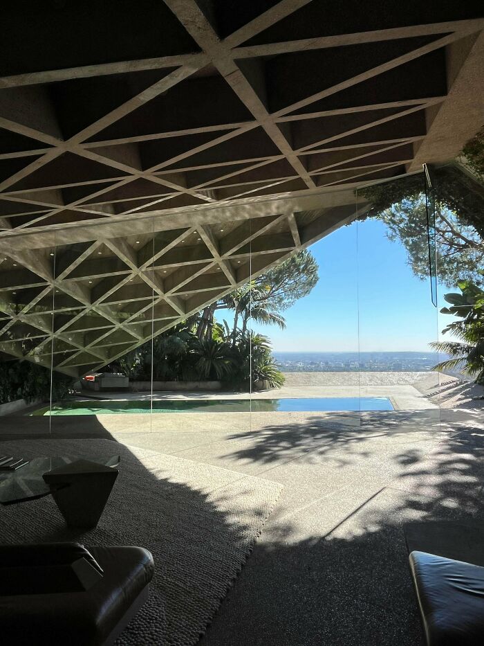 Architecture lovers will appreciate this view of a geometrically patterned concrete roof extending over a pool with a city panorama.