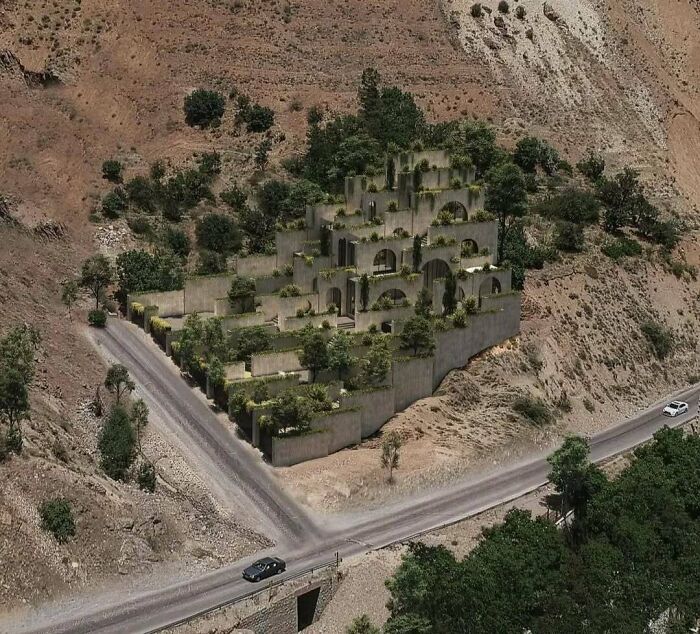 Impressive terraced architecture lovers building with lush greenery integrated into the concrete structure, nestled in a dry, mountainous landscape.