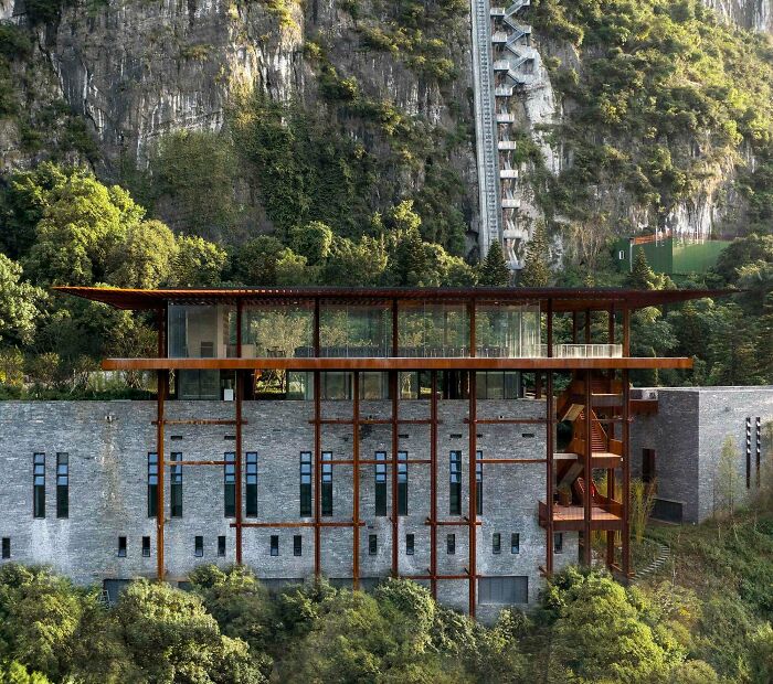 An impressive building with a vast glass upper floor and a textured stone lower section, nestled against a lush, rocky cliff. Architecture lovers will appreciate its unique design.