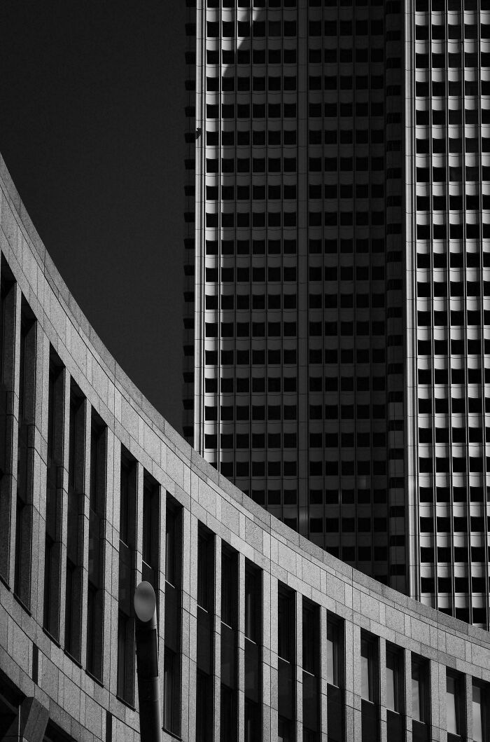 Black and white photo showcasing contrasting architecture: a curved building in the foreground and a towering skyscraper in the background. Architecture lovers will appreciate this.