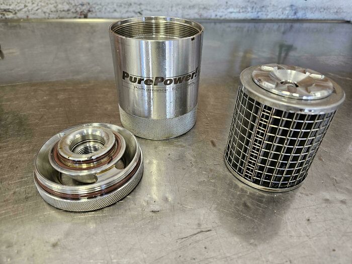 Car mechanics showing detailed parts of a PurePower filter component on a metal workbench surface.