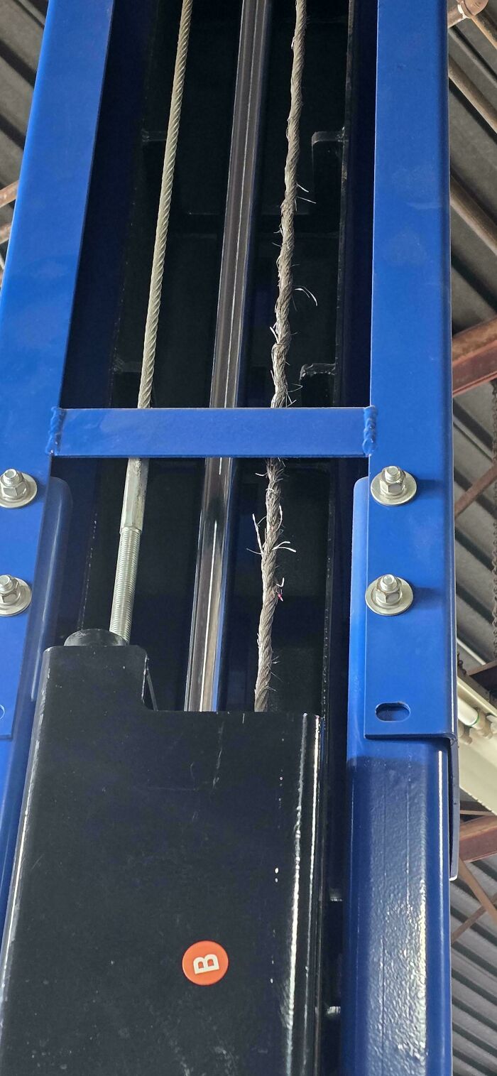 Close-up of frayed cable on car lift showing worn mechanic equipment needing urgent repair in auto shop.