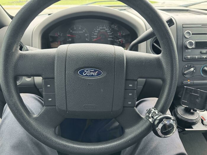 Steering wheel inside a Ford vehicle with control buttons and a steering k**b, showing car mechanics' perspective.