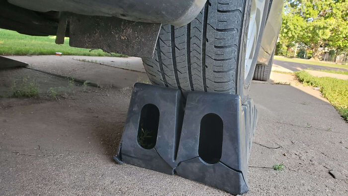 Car mechanics taking a photo of a tire lifted on plastic ramps to show the unusual lifting setup clearly.