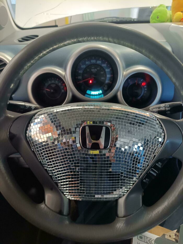 Car mechanics photo showing a unique mirrored disco ball steering wheel cover on a Honda dashboard.