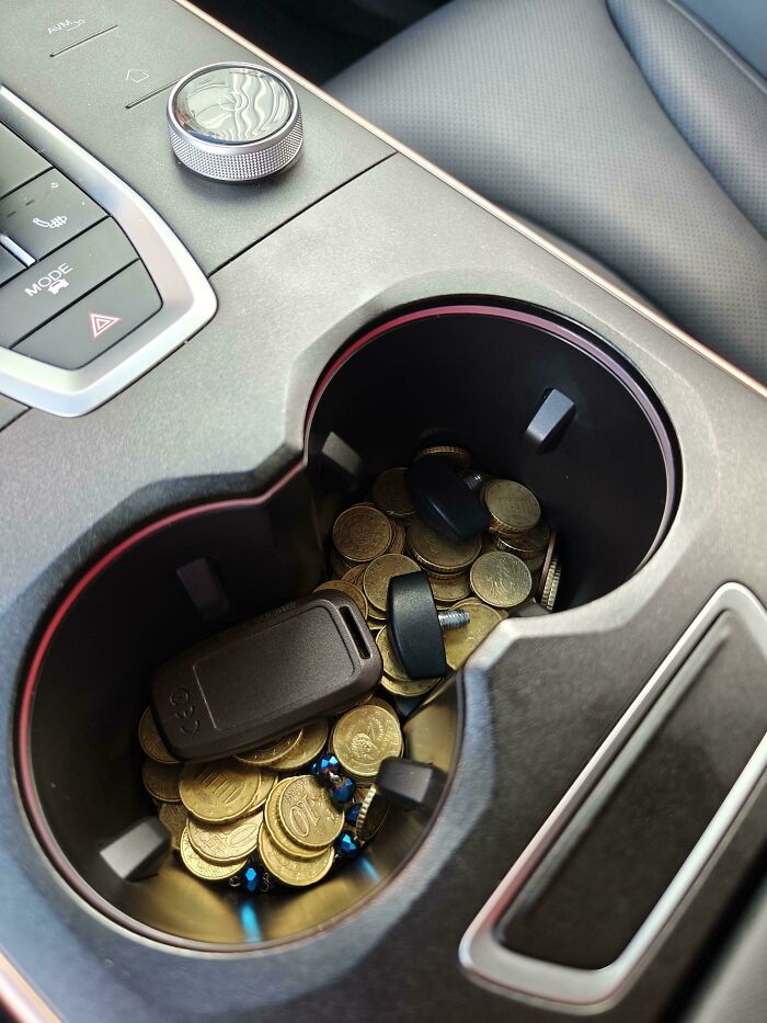 Car mechanics showing a close-up of a car cup holder filled with coins and a car key to prove their work.
