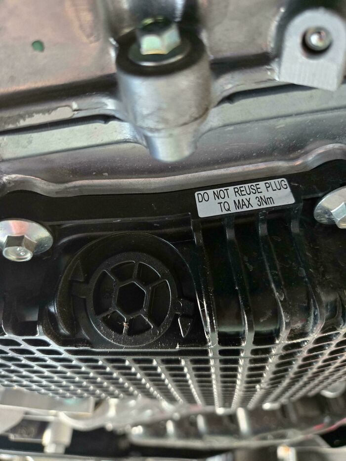 Close-up of a car engine component with a warning label about torque limits and plug reuse for car mechanics.