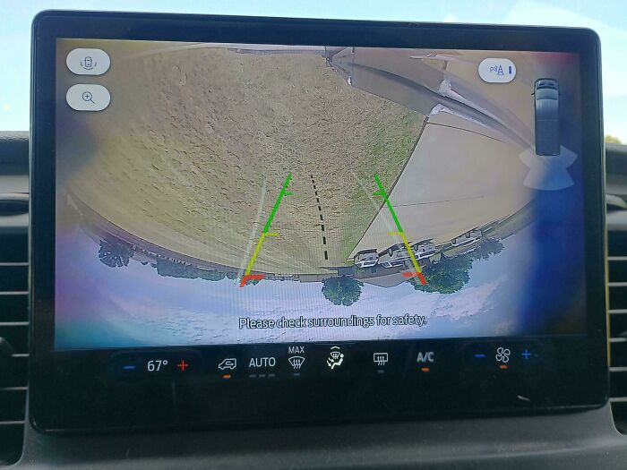 Car mechanics view backup camera display showing parking guidelines and surrounding area for safety while reversing.