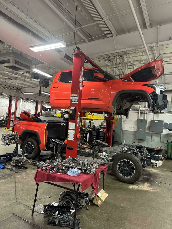 Red Toyota Tundra lifted in a mechanic shop with engine and parts removed for repair and inspection.