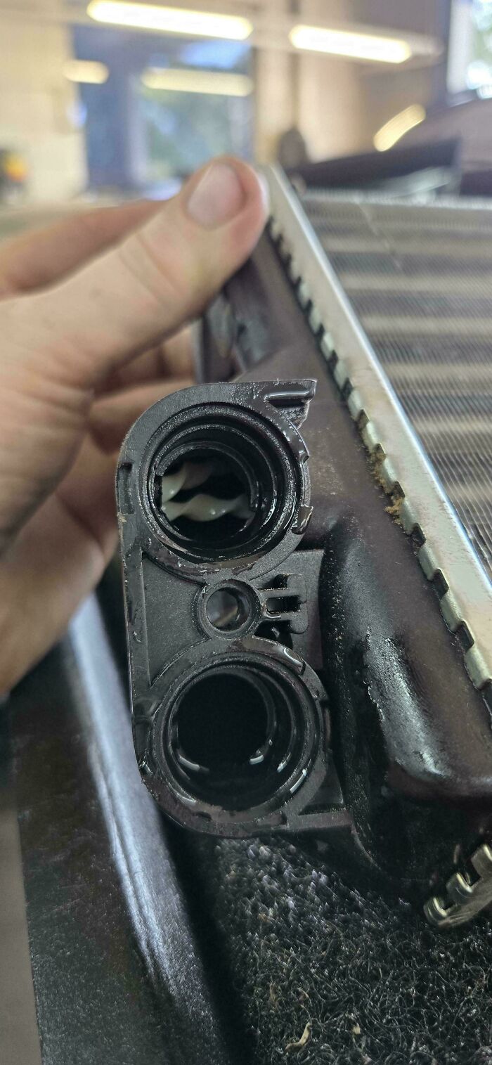 Close-up of a car mechanic holding a damaged radiator component showing internal corrosion and debris.