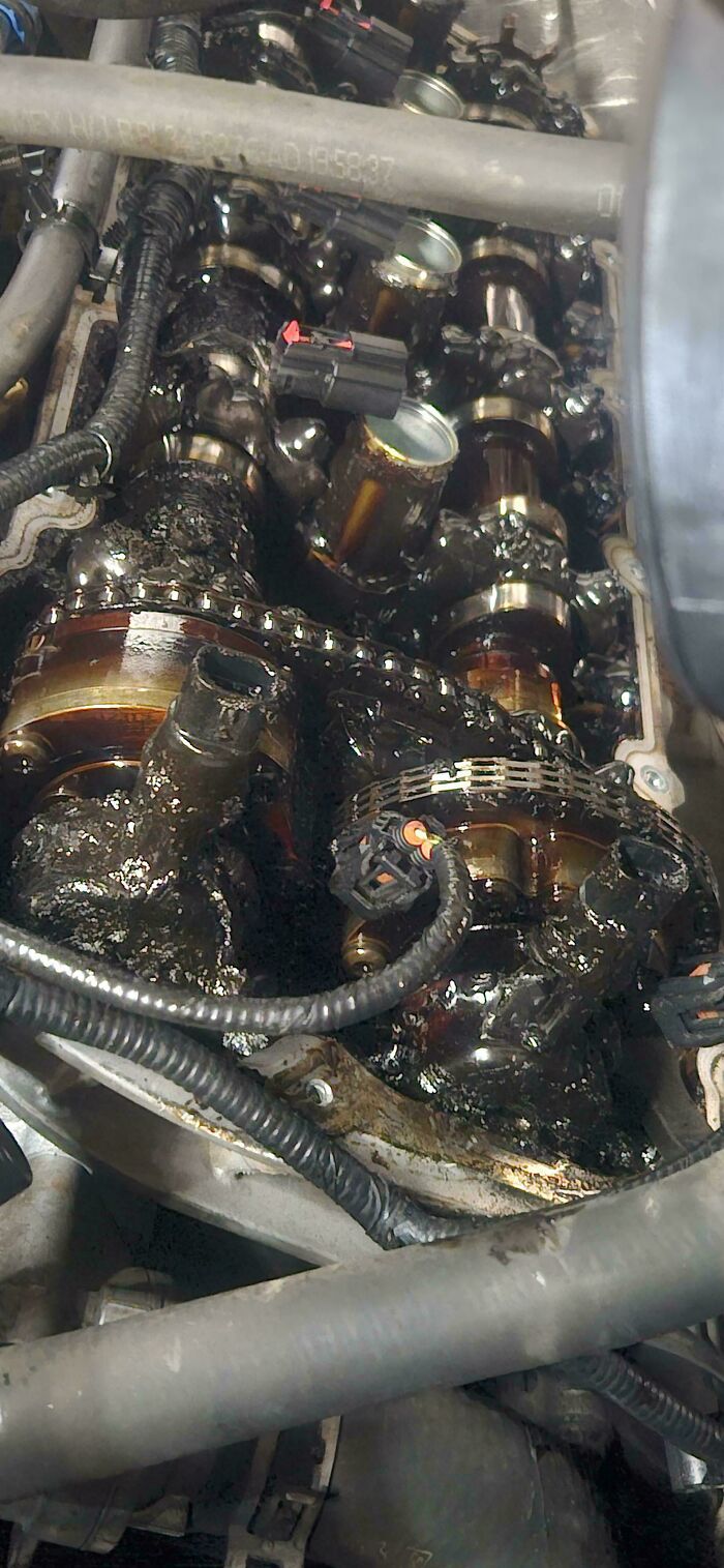Close-up of a car engine with camshaft covered in thick, black sludge during mechanic inspection for repair.