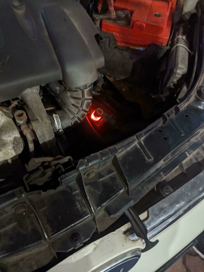 Close-up of a car engine compartment with a red battery and visible mechanical components for car mechanics.