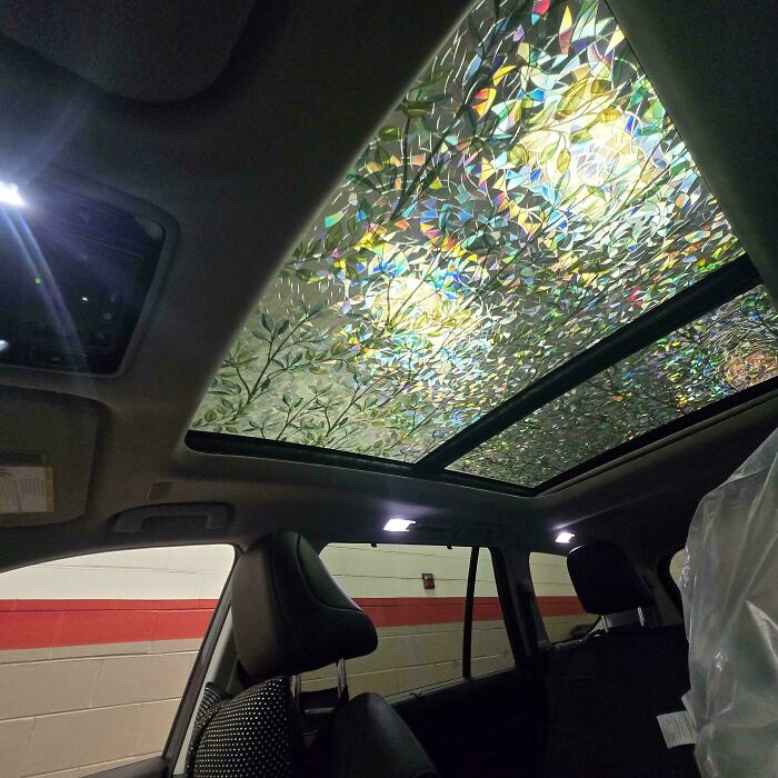 Car mechanics capturing a photo of a car’s panoramic sunroof with a broken, shimmering glass pattern inside the vehicle.