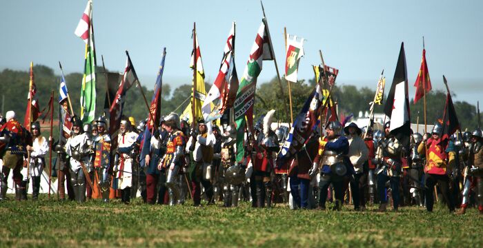 A large group of knights and soldiers in armor, carrying many colorful flags, recreating a scene from the Middle Ages.