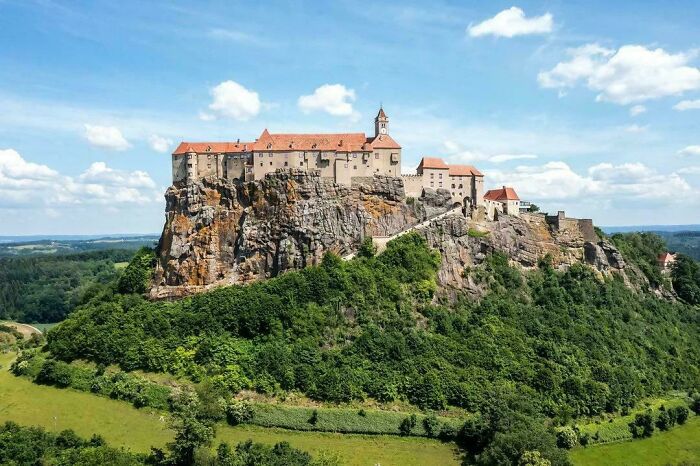 An impressive aerial view of a grand castle perched atop a rocky hill, showcasing Middle Ages architecture.