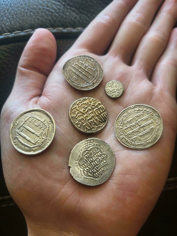 A hand holding several old, engraved coins, tangible pieces of human history from the Middle Ages.