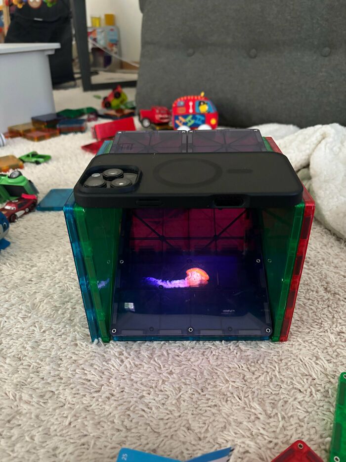 A phone placed on colorful magnetic blocks displaying a glowing jellyfish, illustrating a wholesome, funny, and goofy dad activity.