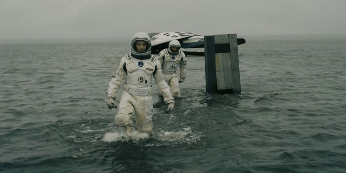 Two astronauts in spacesuits wading through water with a spaceship in the background, a nonsensical movie detail.