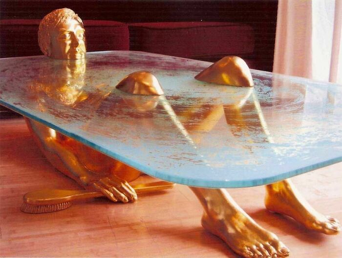 Ridiculous piece of furniture featuring a golden human figure supporting a glass tabletop in a living room.