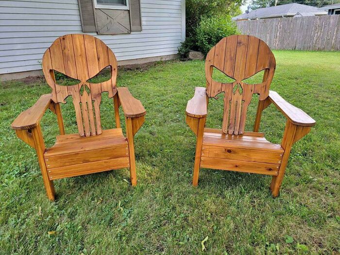 Two wooden chairs with Punisher skull design backs placed on a grassy lawn as unusual pieces of furniture.