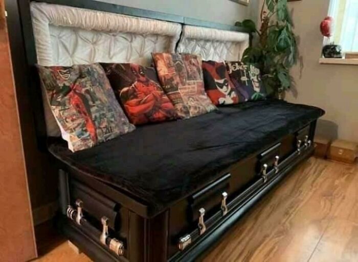 Unique furniture piece designed as a couch made from black coffins with cushions and a padded backrest.
