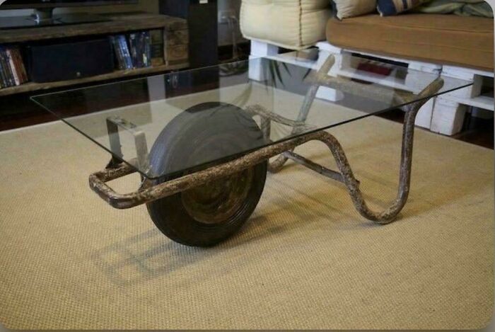 Glass tabletop coffee table made from a repurposed wheelbarrow, showcasing a ridiculous piece of furniture design.