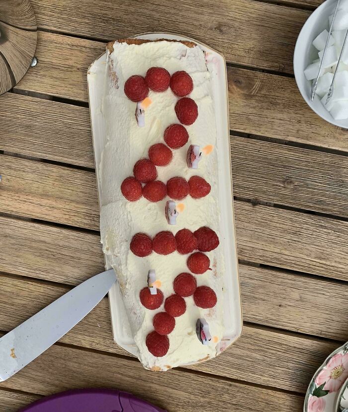 Raspberry cake with number 2 formed by berries and lit birthday candles on a wooden table showing entitled family moment.