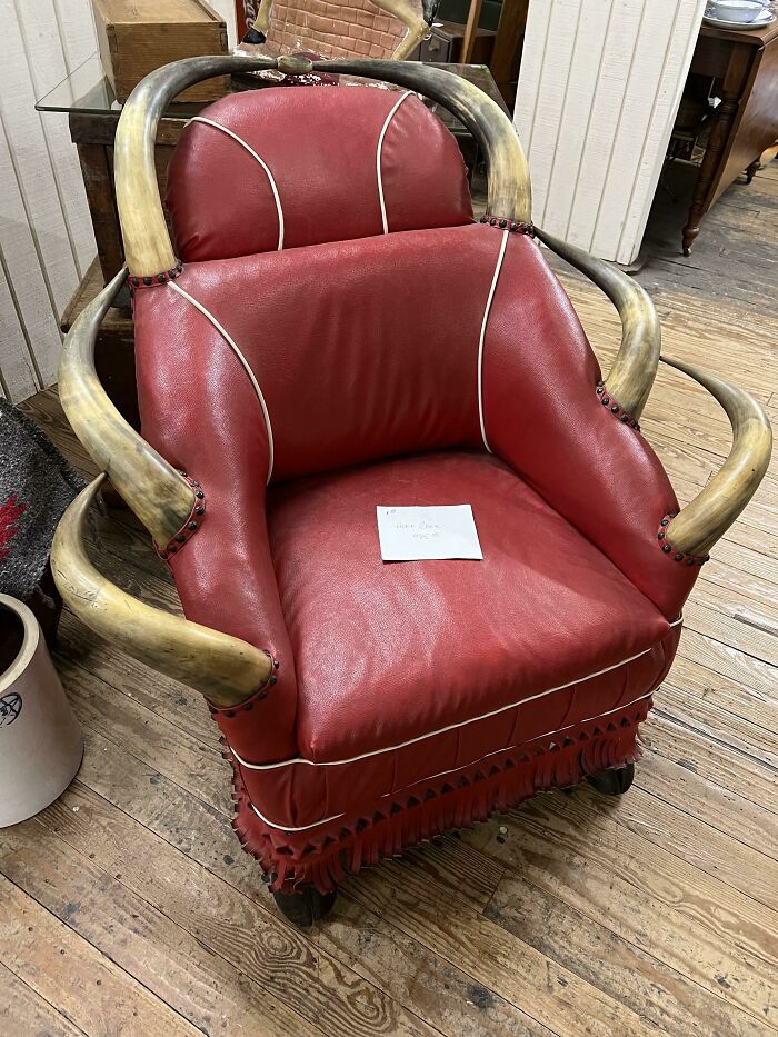 Red leather chair with curved horn-like wooden armrests on a worn wooden floor, showcasing ridiculous pieces of furniture.