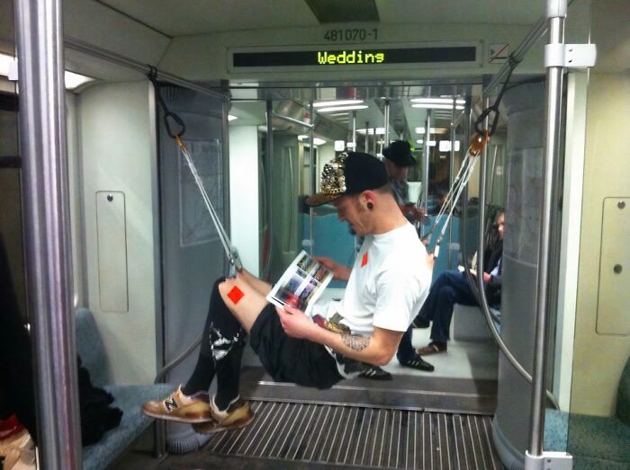 Man suspended by straps inside NYC subway car, reading a book in a bizarre and weird subway moment.