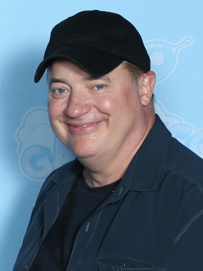 Smiling iconic actor wearing a black cap and dark jacket against a blue background, representing actors who vanished from Hollywood.