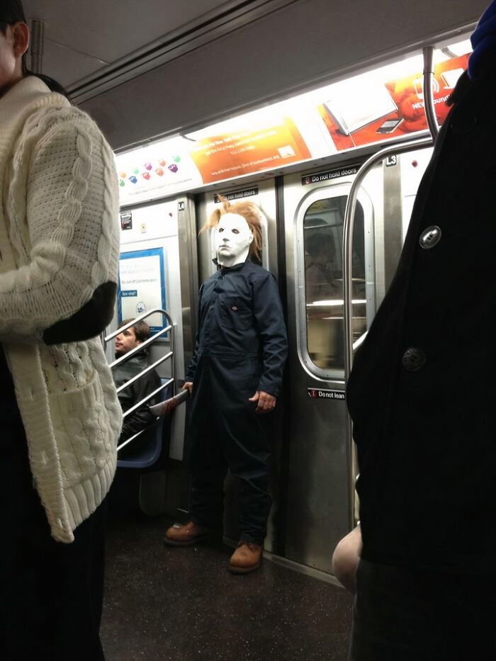 Person wearing a spooky mask and costume holding a bat inside NYC subway during a weird moment on the subway.