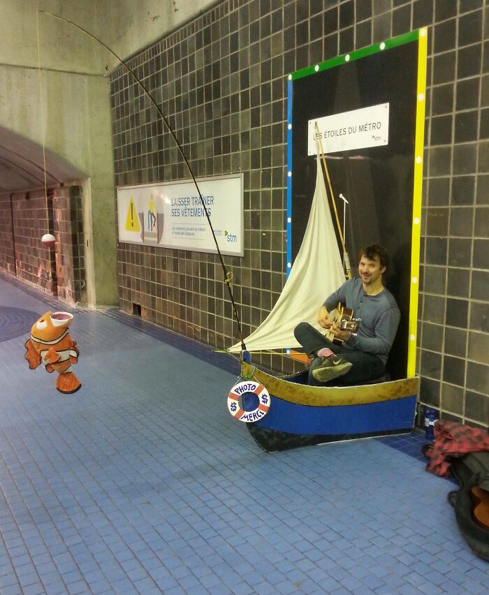 Man playing guitar sitting in a small boat with fishing pole and clownfish in a subway, a weird moment on the NYC subway.