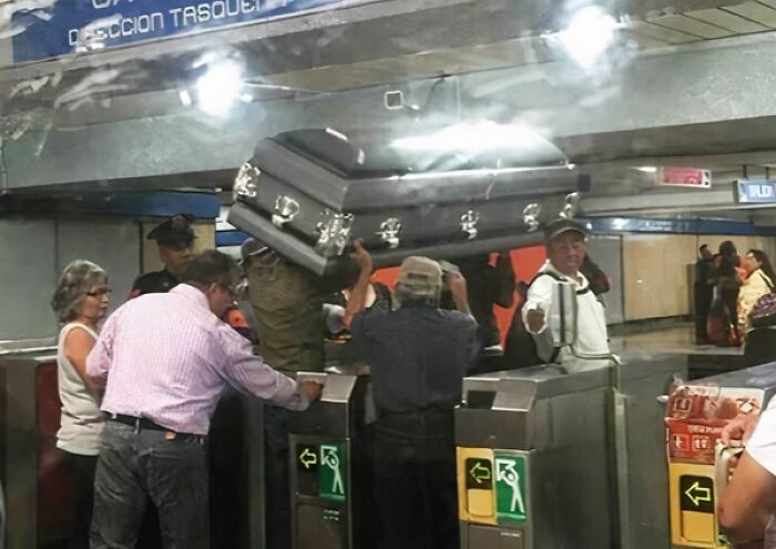 People carrying a large coffin over turnstiles in a crowded NYC subway station during a strange moment.