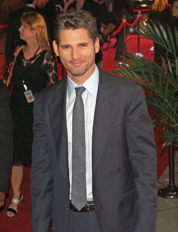 Male actor in a dark suit and tie posing on a red carpet event, representing iconic actors who vanished from Hollywood.