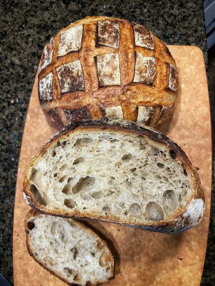 Rustic sourdough bread with a scored crust and airy crumb displayed on a wooden cutting board, showing food common everywhere.