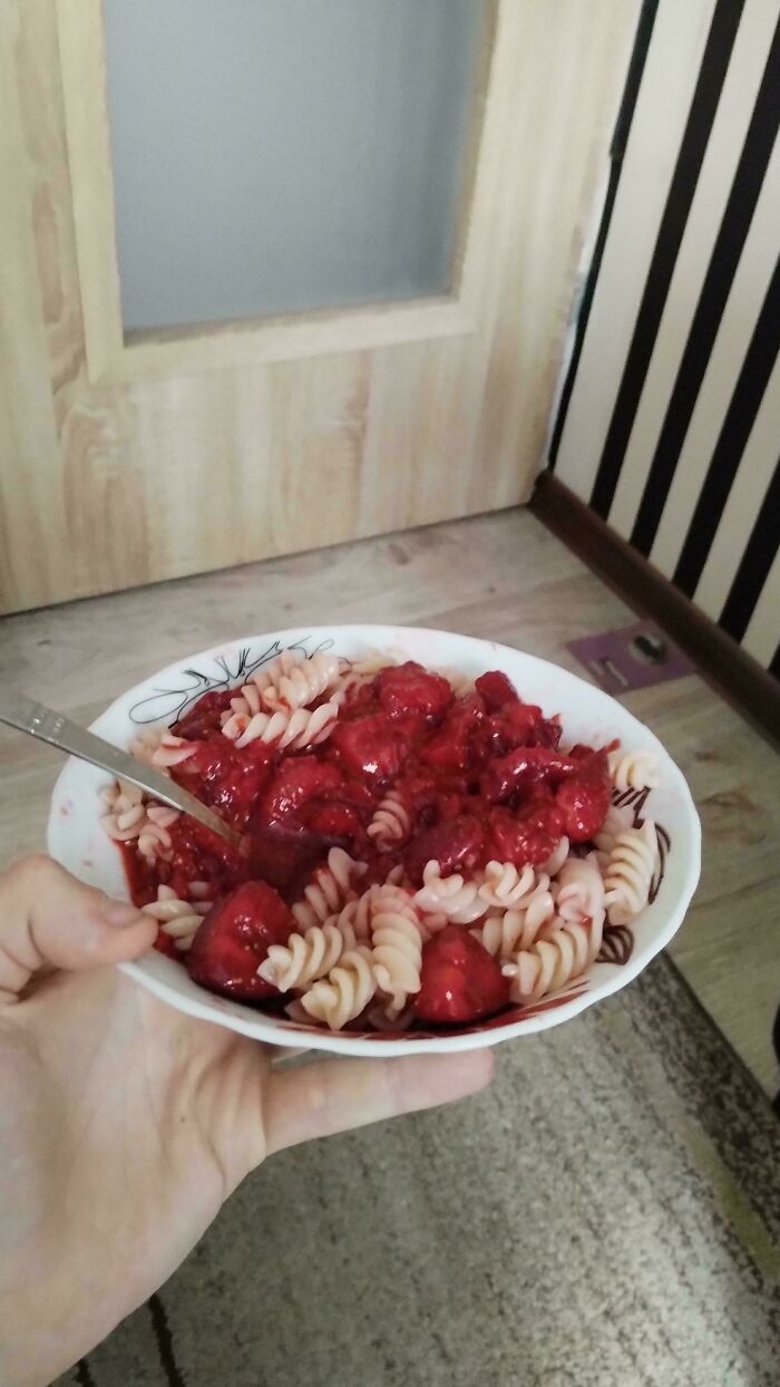 Hand holding bowl of pasta with red fruit sauce indoors showing unique food people think is common everywhere.