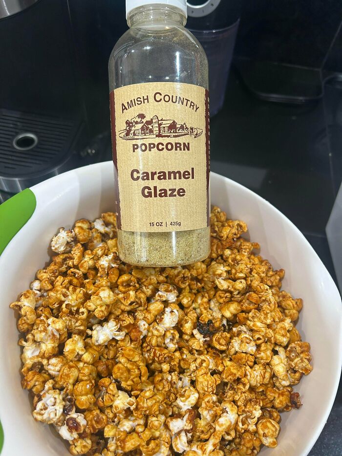 Bottle of Amish Country caramel glaze held above a bowl of caramel popcorn, showing a unique snack from different countries.
