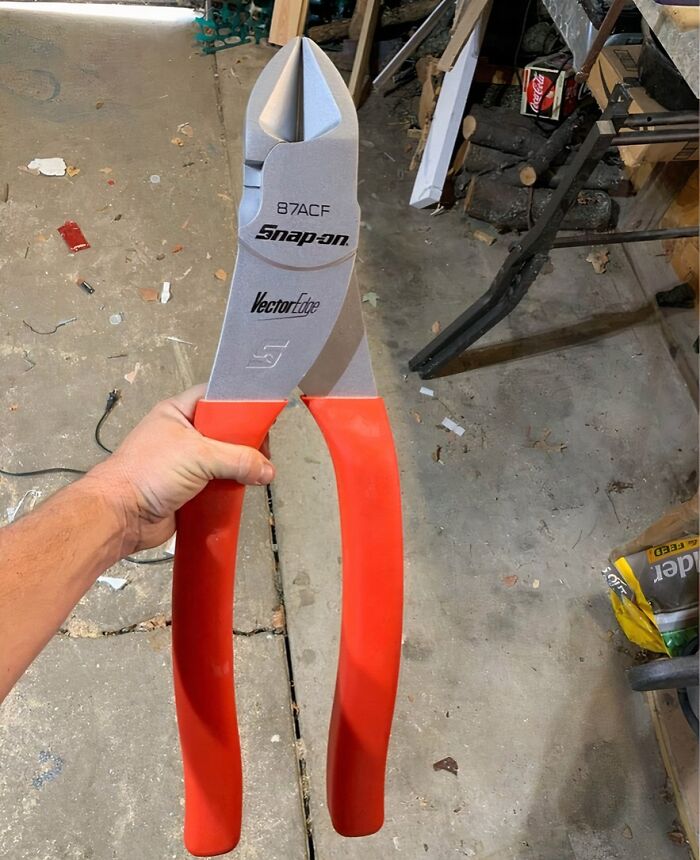 Hand holding Snap-on Vector Edge pliers with red handles in a workshop, showcasing interesting tools for problem solving.