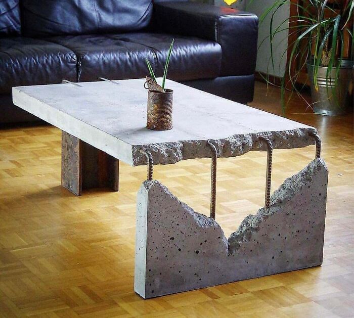 Concrete furniture table with rugged edges and metal rods, showcasing a unique and unusual design in a living room setting.