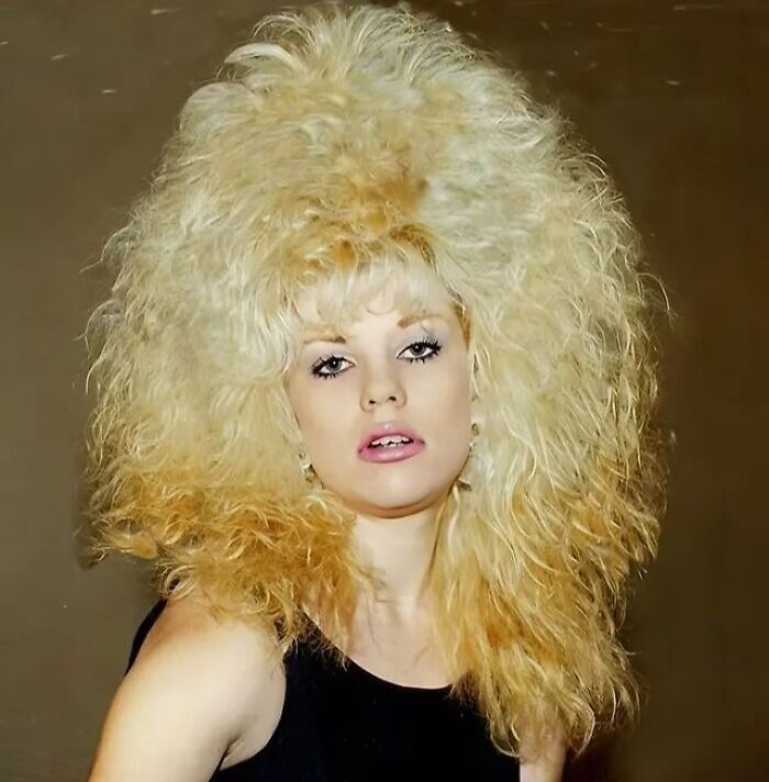 Blonde woman with an iconic 80s hairdo featuring large, teased, voluminous curly hair in a dramatic style