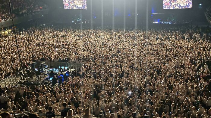 Massive crowd at an indoor concert with lighting rigs and stage equipment, showcasing incredible moments in reality.