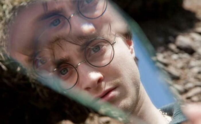 Close-up of a man with round glasses reflected in a broken mirror, illustrating absurd movie and TV details.