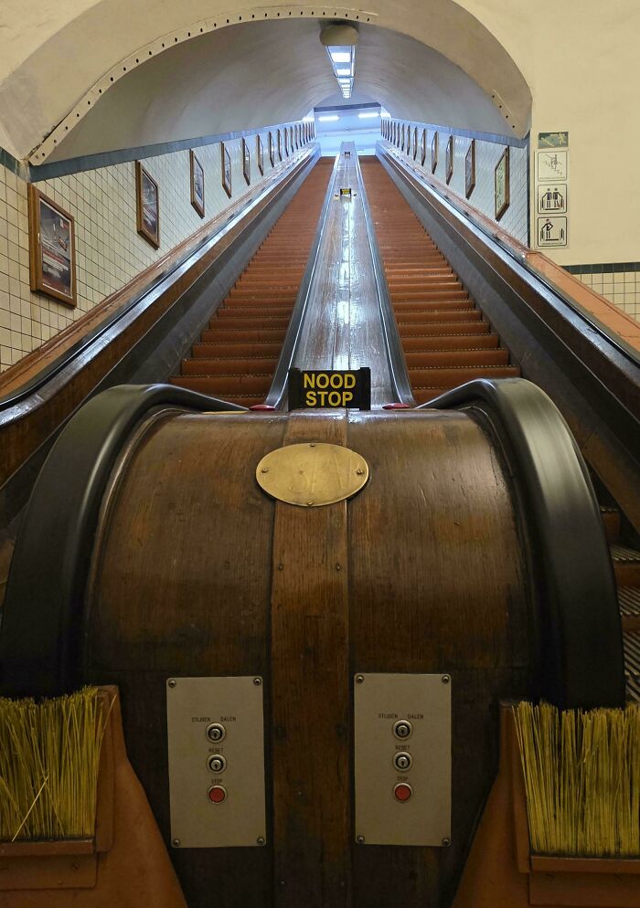 A long, vintage escalator with beautiful architecture, featuring wooden handrails and a NOOD STOP sign.