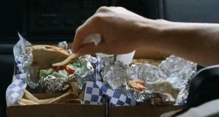 Hand reaching for fries among foil-wrapped food containers showing hilariously absurd movie and TV details.