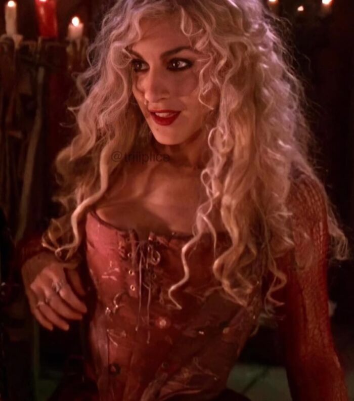 Woman with curly blonde hair wearing a vintage corset in a dimly lit setting, illustrating absurd movie and TV details.