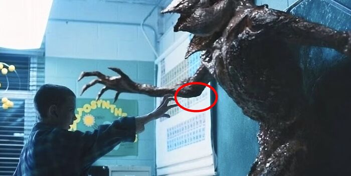 Boy in a blue plaid shirt reaching out to a monster’s claw in a dimly lit room, showing absurd movie details.